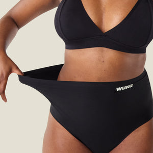 Woman stretching waistband of WUKA High Waist Period Pants in black to show flexibility, demonstrating adaptable fit and comfort for all body types.