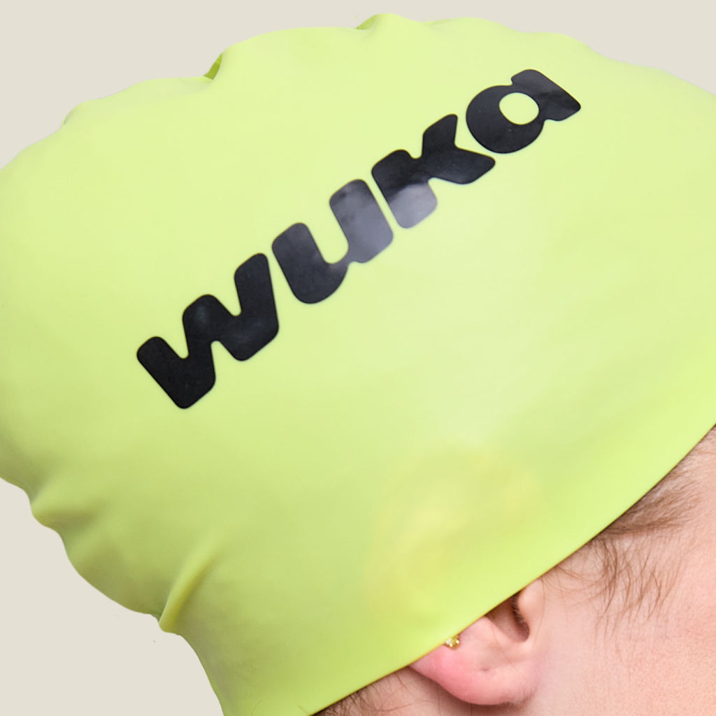 Close-up of WUKA swim cap logo on lime punch silicone surface, highlighting premium quality.