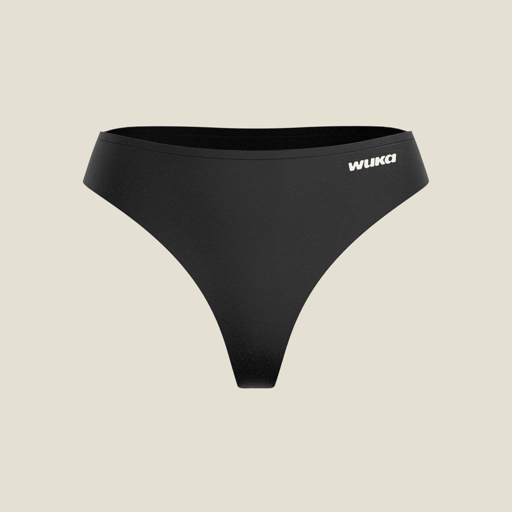 Front view of the black WUKA Stretch Seamless Mid Period Thong for light flow on its own against a cream background, with the white WUKA logo on the front.